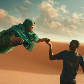 In der Wüste: Mann hält schwebende Frau an der Hand