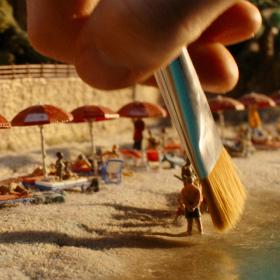 Miniaturfiguren am Strand werden mit einem Pinsel bearbeitet